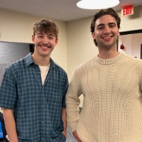 Two boys smile at the camera with their hands on their hips.